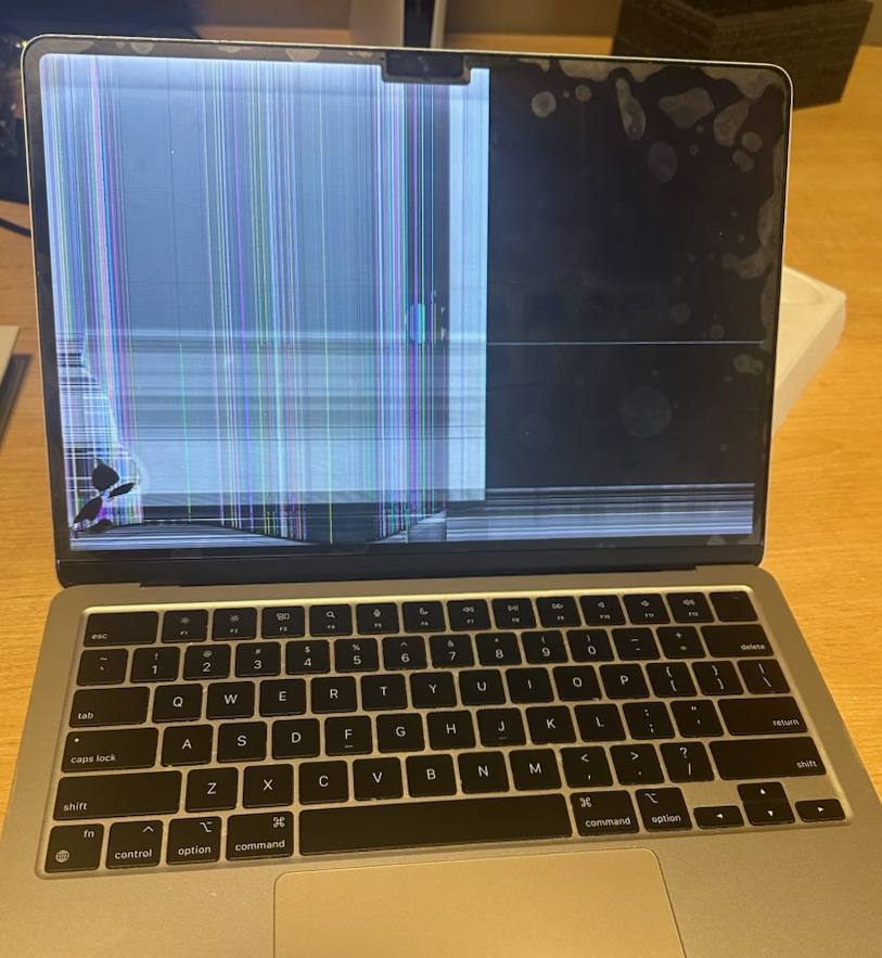 MacBook with damaged display showing vertical lines and a cracked lower corner